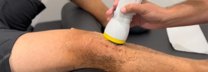 SoftWave therapy applicator positioned on a patient’s knee with gel applied during a treatment session.