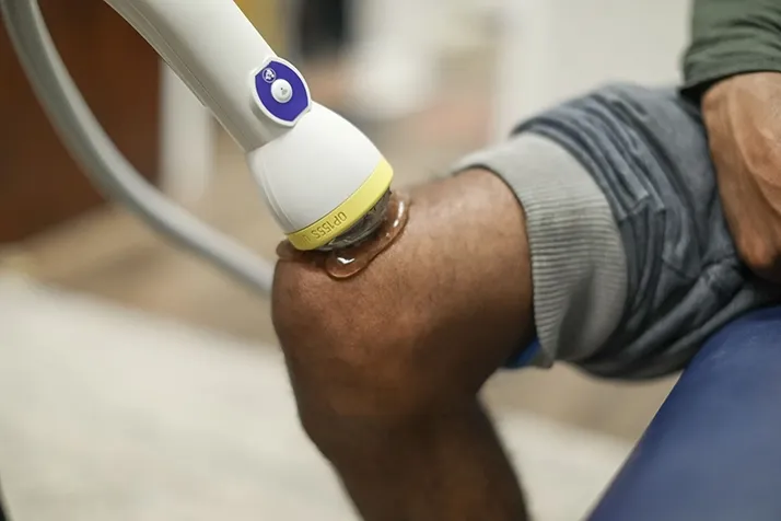 SoftWave therapy applicator positioned on a patient’s knee with gel applied during a treatment session.