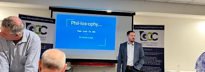 Presenter standing beside a display screen showing educational content during a classroom-style presentation.