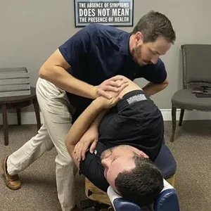 Dr. Dusty Large performing a side-posture spinal adjustment on a patient positioned on a chiropractic treatment table.