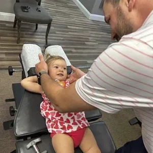 Dr. Dusty Large placing hands near a child’s head while the child lies on a chiropractic treatment table.
