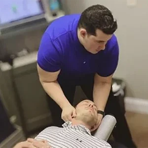 Dr. Eduardo Emanuel Rivera performing a cervical adjustment on a patient lying on a treatment table in a clinical room